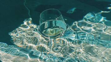 A glass of white liquid, possibly wine, floating on water with ripples and reflections.