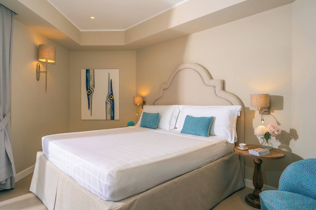 A hotel room with a large bed, two bedside lamps, a small table with a vase of flowers, and a blue chair.