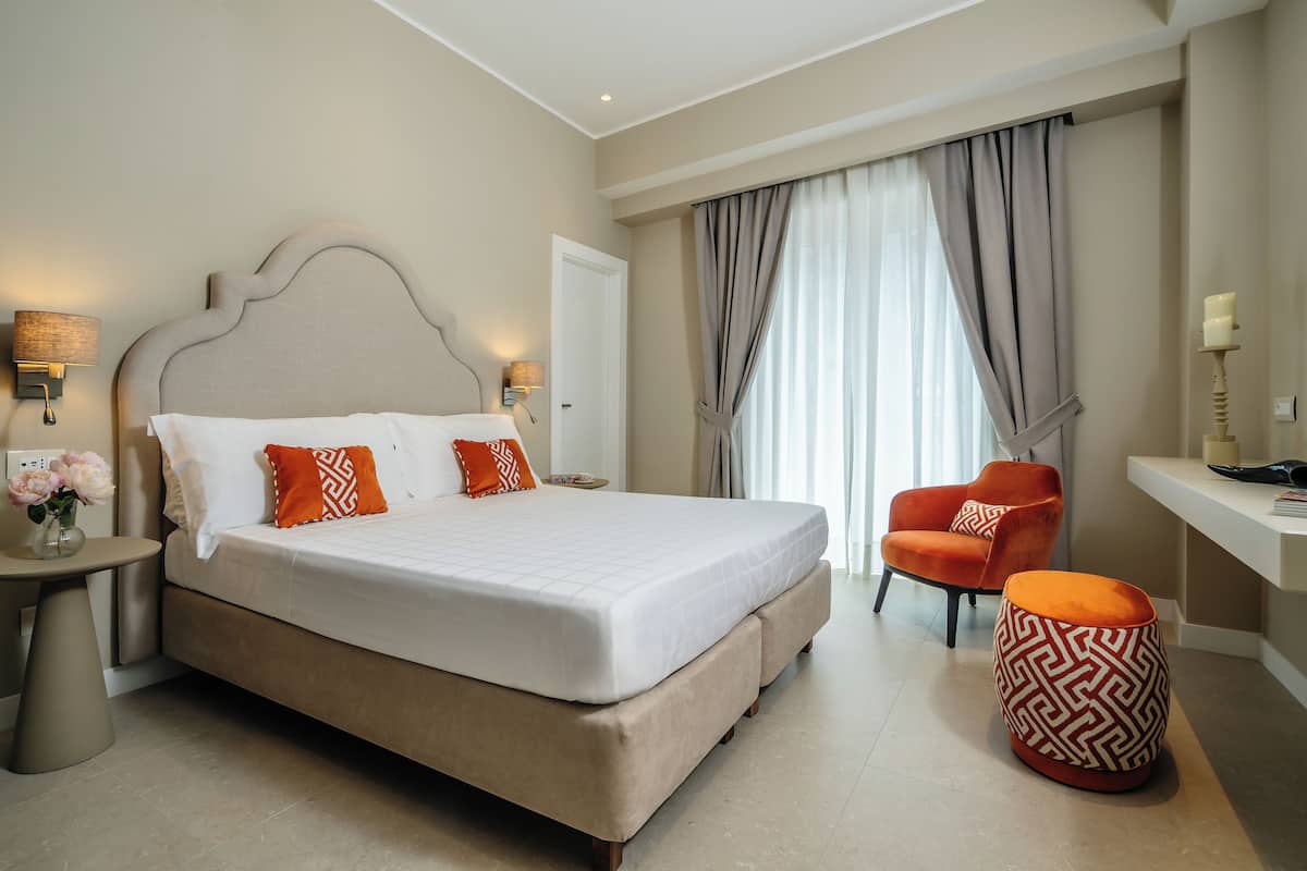 A hotel room with a large bed, a chair, a small table, and a decorative ottoman.