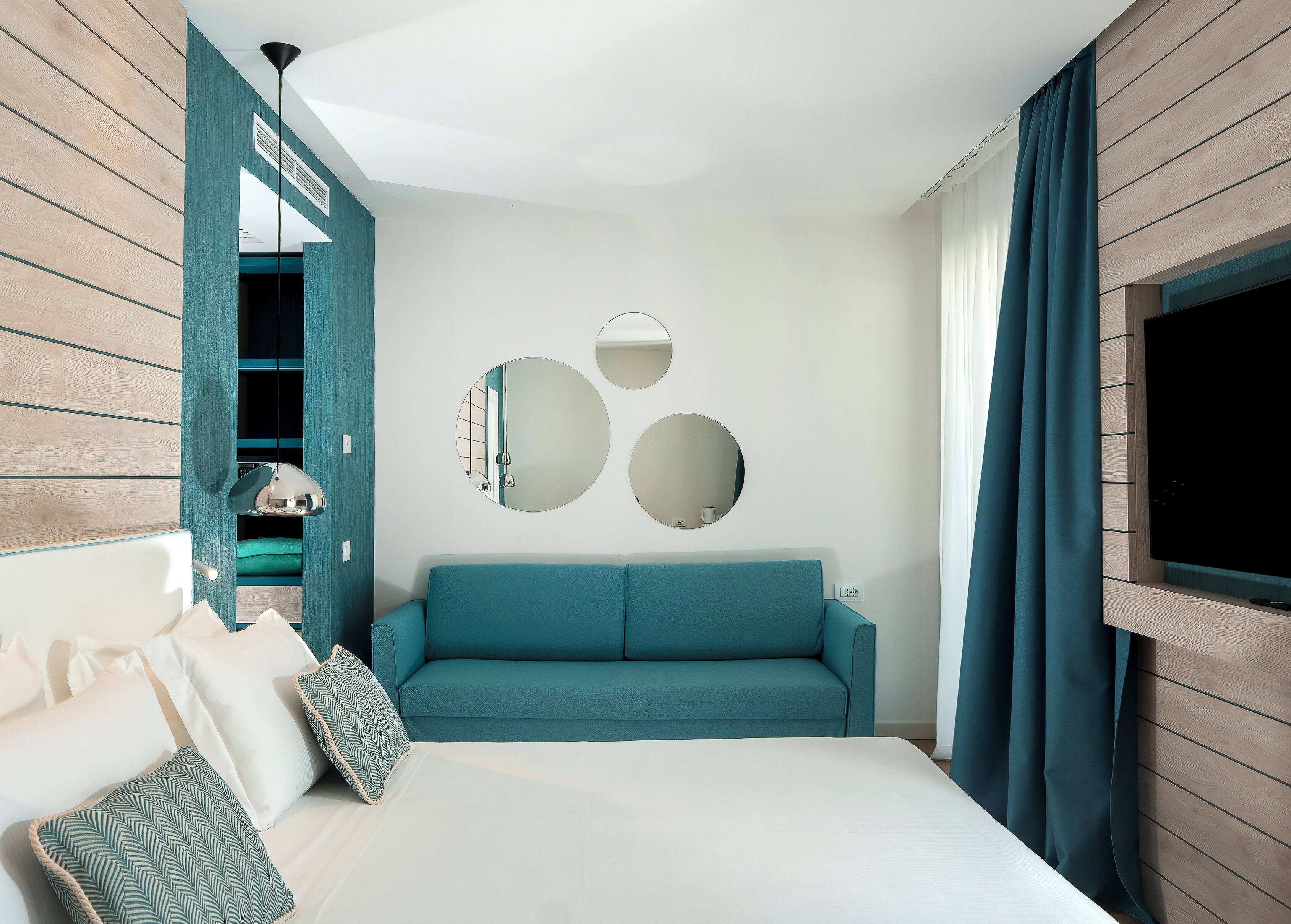 A modern hotel room with a large bed, teal sofa, and two wall-mounted mirrors.
