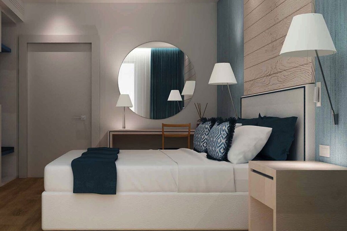 A modern bedroom with a large bed, bedside lamps, a round mirror, and a wooden accent wall.