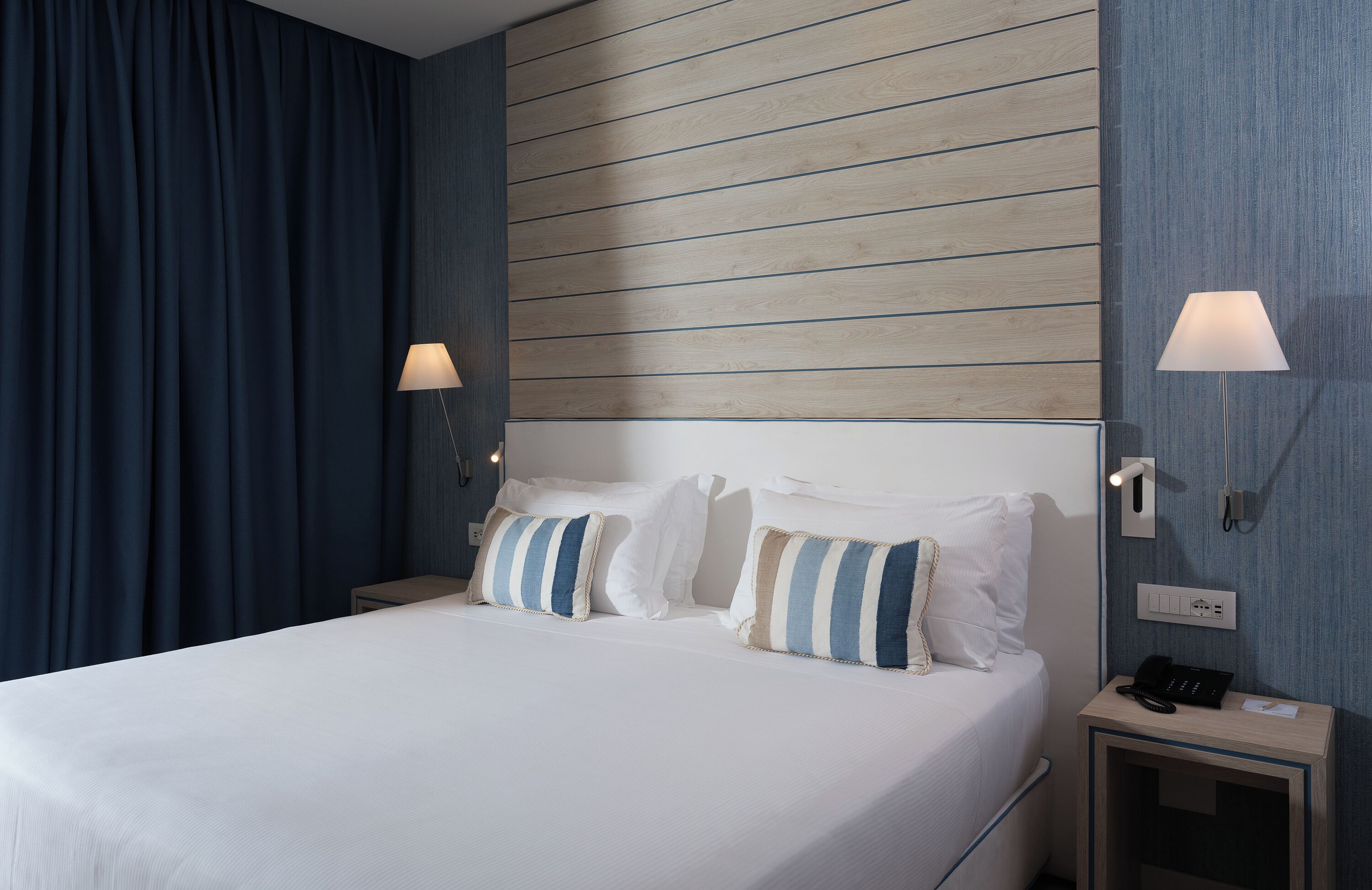 A hotel room with a bed, two bedside tables, a lamp, and a telephone.