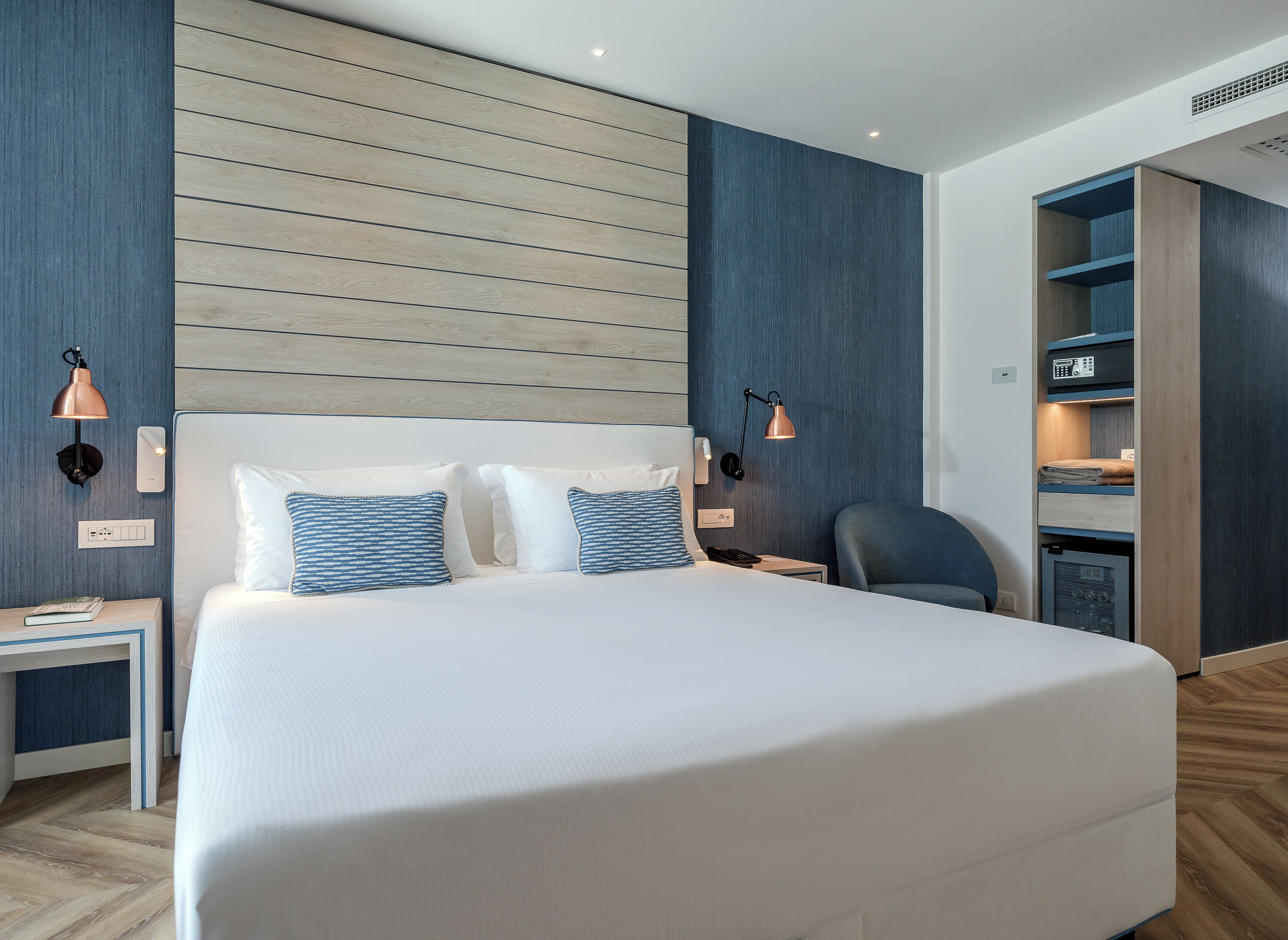 A modern hotel room with a large bed, bedside lamps, a desk, and a built-in wardrobe.