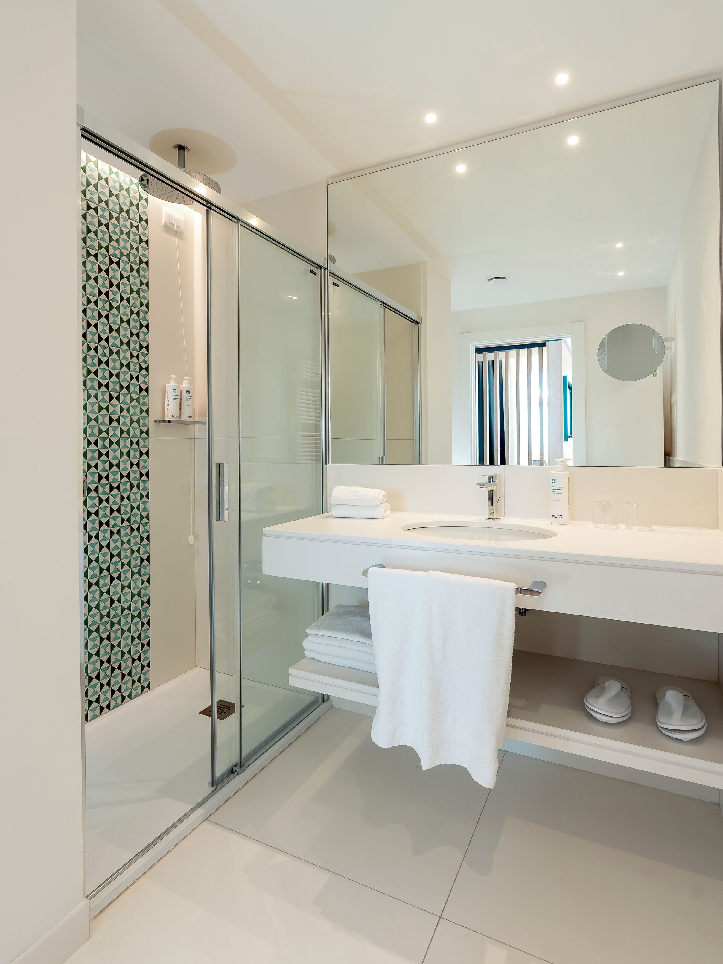 Un bany modern amb una cabina de dutxa de vidre, un lavabo blanc i un mirall, i tovalloles nítidament dobles.
