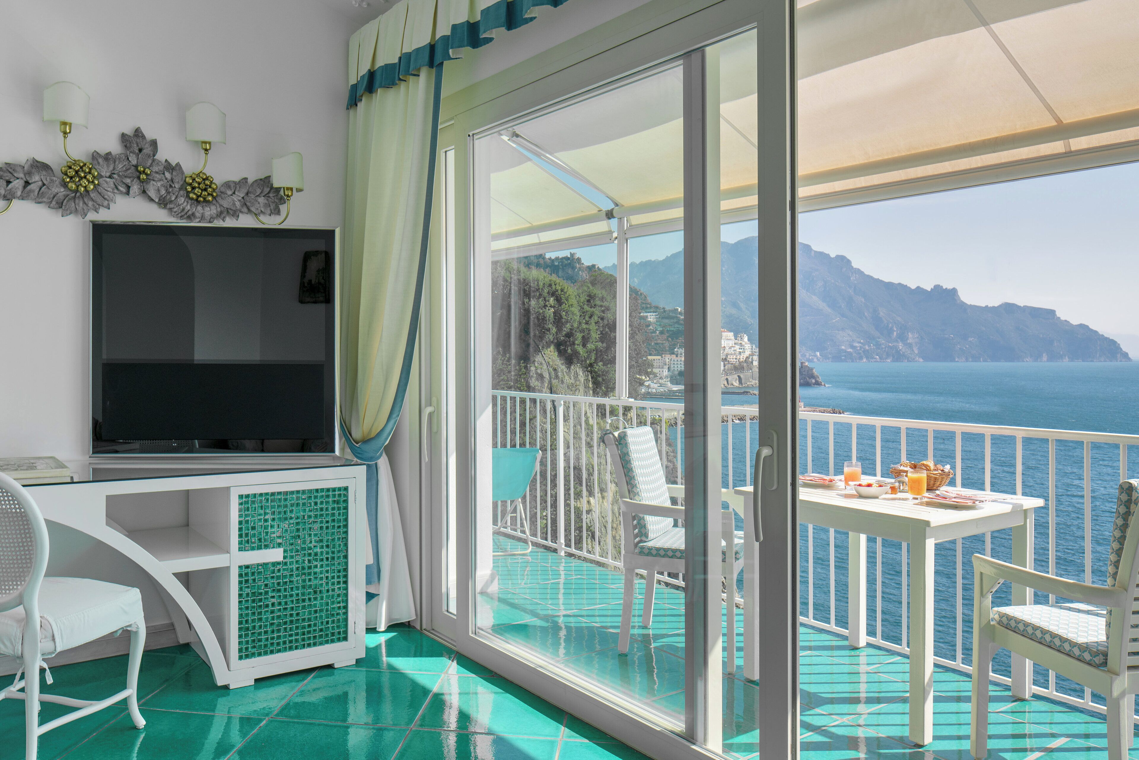 A balcony with a TV, chairs, and a table with breakfast items.