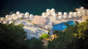 Vista aérea de un complejo turístico con piscina central, sillas de sol, sombrillas y una terraza de madera.