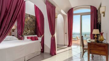 A hotel room with a bed, a desk, and a view of the sea.