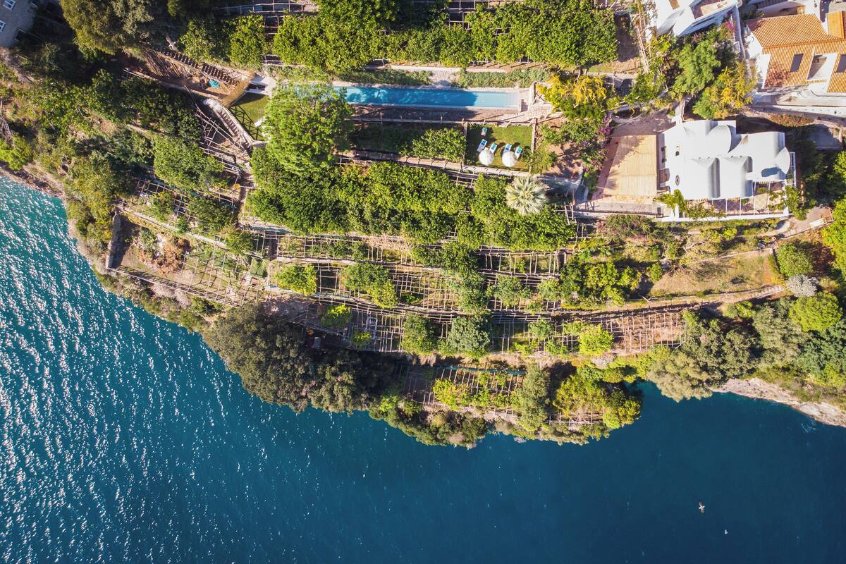 Ein Luftbild eines Küsteneigentums mit Schwimmbad, terrassierten Gärten und einem großen Gebäude.