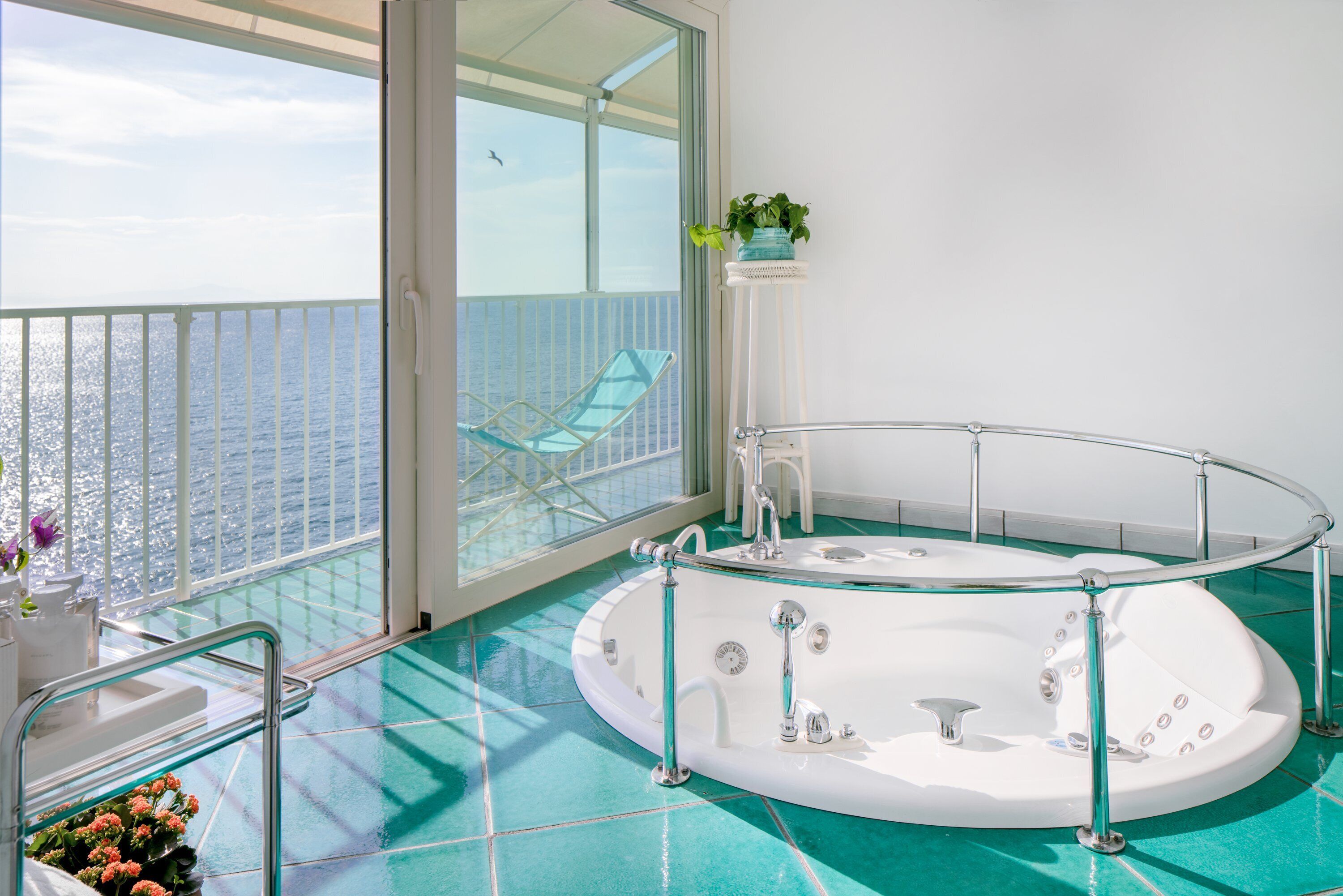 A balcony with a glass balustrade, a white bathtub, and a view of the sea.