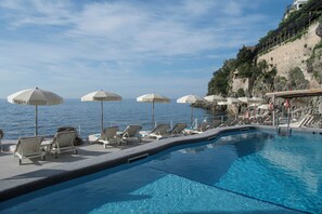 A poolside area with lounge chairs and umbrellas, overlooking a body of water and a rocky hillside. - Santa Caterina (Amalfi)