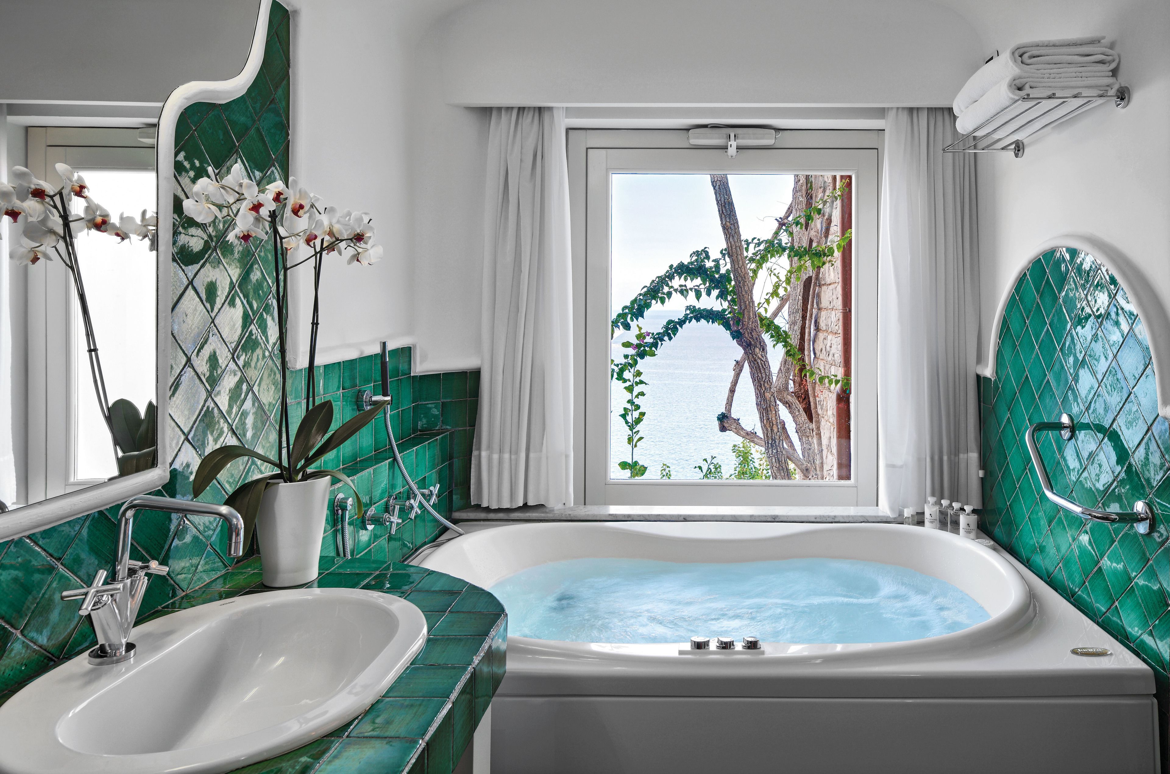 Une salle de bain avec une baignoire, un lavabo et une vue sur la mer par une fenêtre.