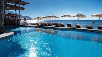 Relax by the serene pool, surrounded by lounge chairs and umbrellas, with the ocean in the background.