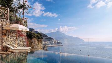 Una piscina infinita con agua cristalina, un muro de piedra y vistas al mar y a las montañas.