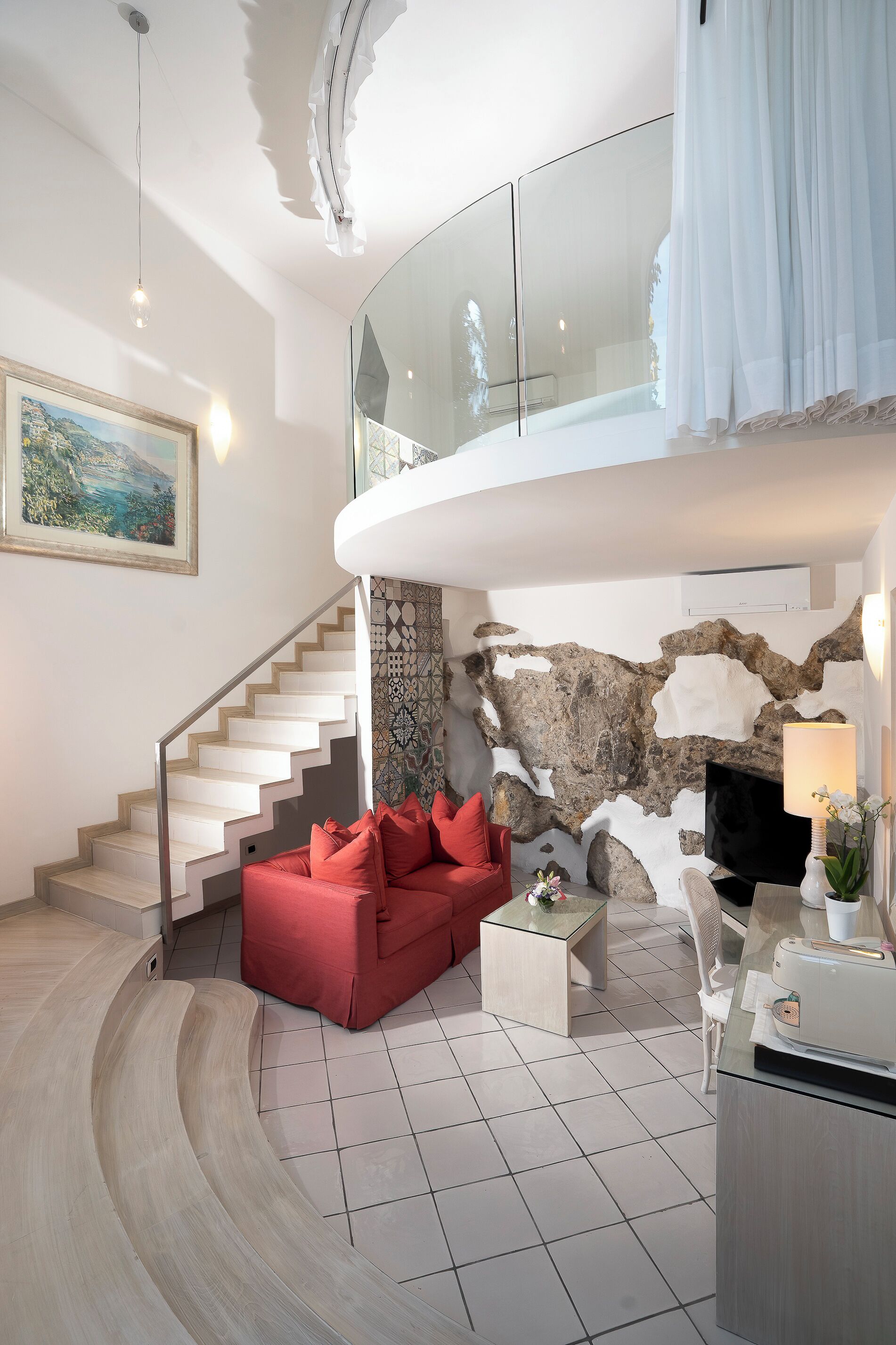Un salon moderne avec un escalier à volutes, un canapé rouge, un téléviseur à écran plat et un mur en pierre.