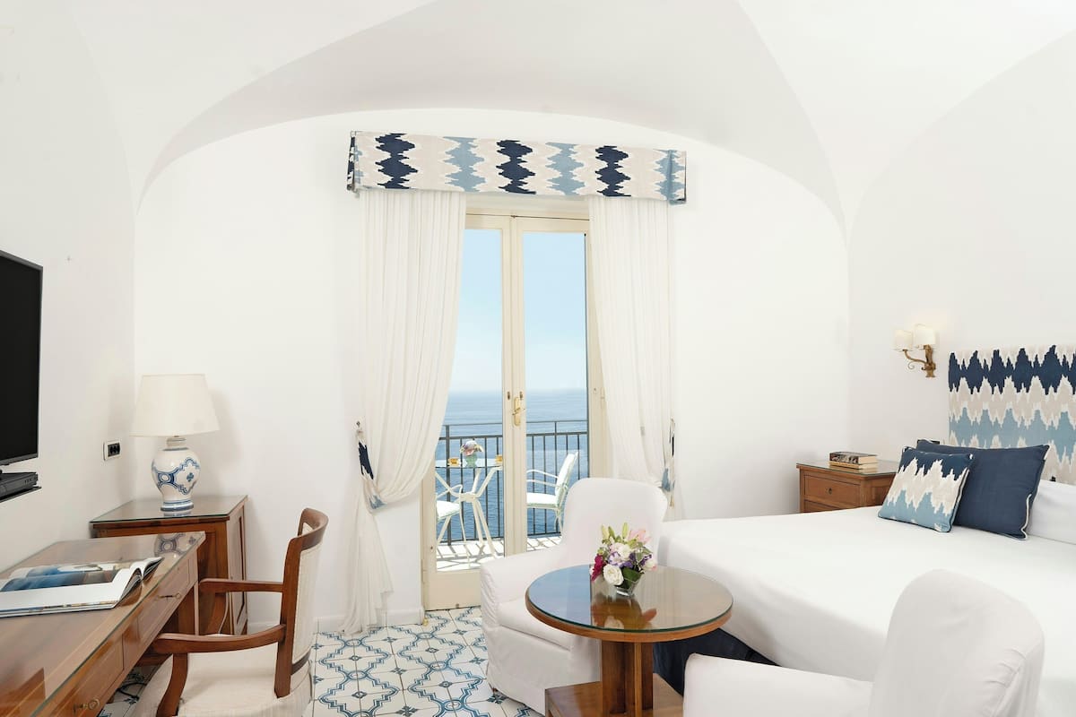 Ein Hotelzimmer mit Balkon, einem Bett, einem Schreibtisch und einem Stuhl.