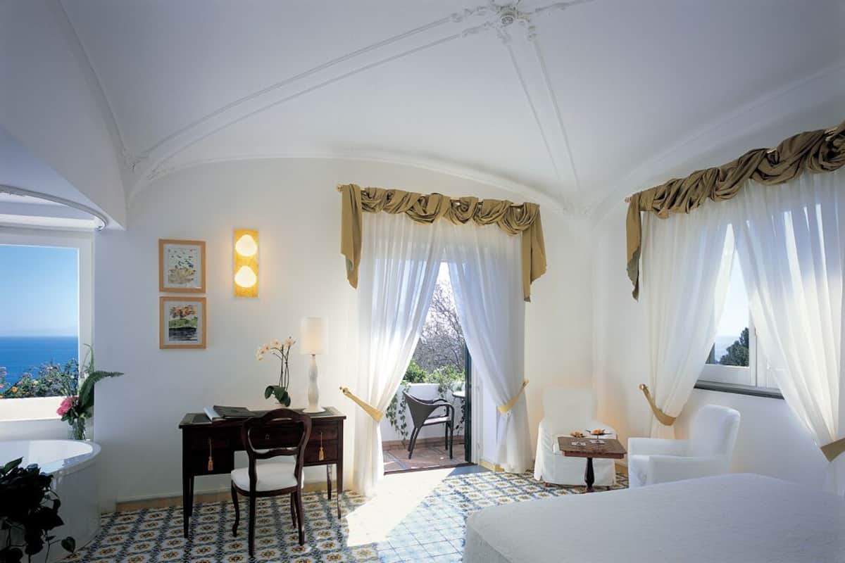 Ein Schlafzimmer mit Bett, Schreibtisch mit Stuhl, Tisch mit Stuhl und Meerblick.