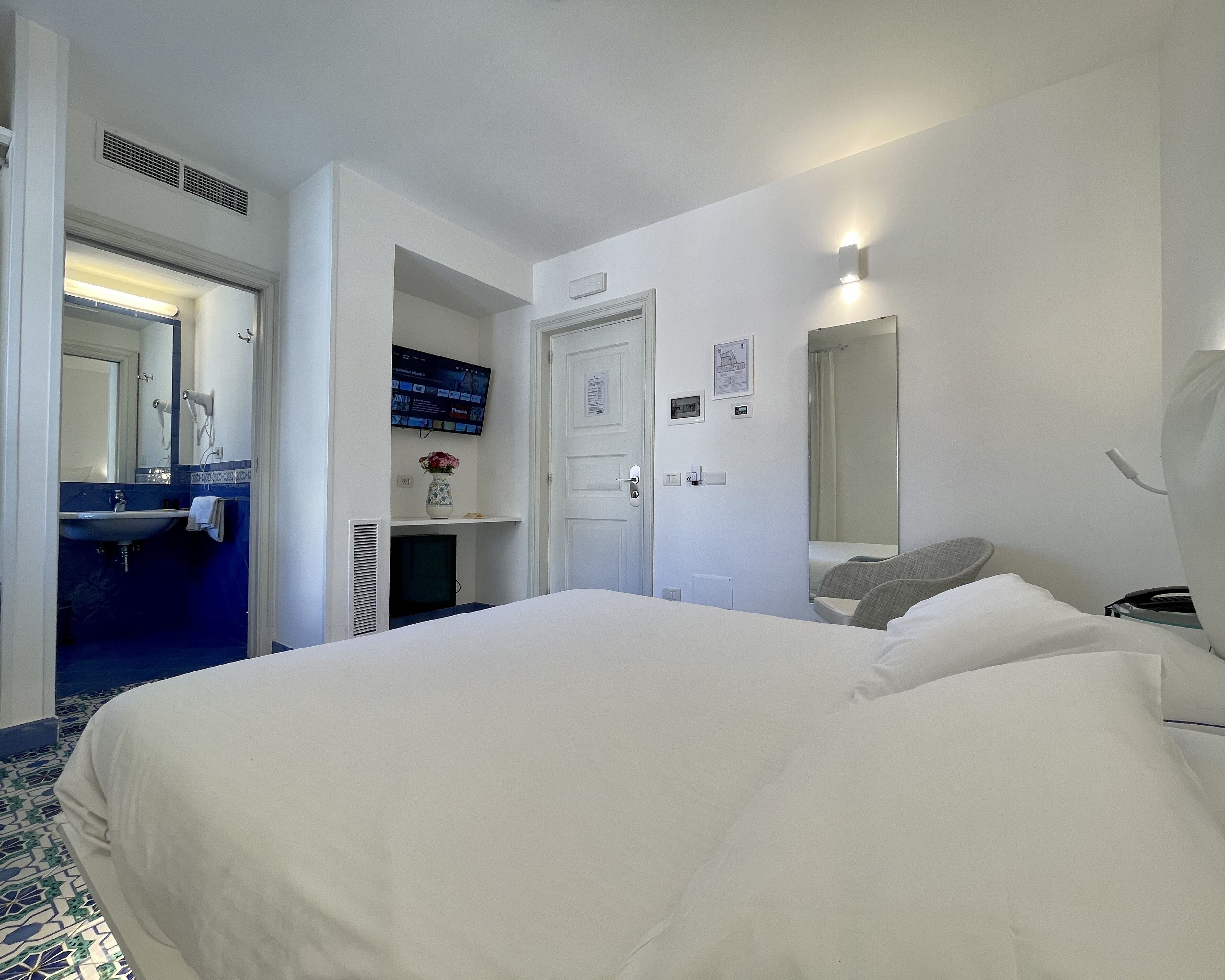 A hotel room with a bed, a bathroom with a sink, a mirror, and a TV on the wall.