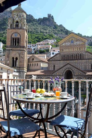 A balcony with a table set for breakfast, overlooking historic buildings and a mountainous backdrop. - Terrazza Duomo (Amalfi)