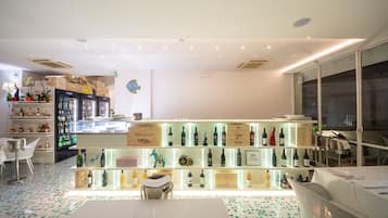 Un espace bar moderne avec des étagères remplies de bouteilles, une table blanche et des chaises.