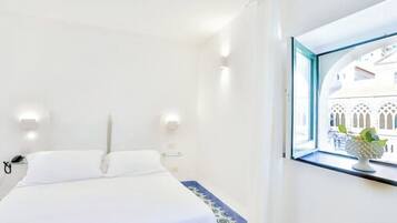 Quarto de hotel com uma cama, uma janela com vista para um edifício e uma pequena mesa com um objeto decorativo.