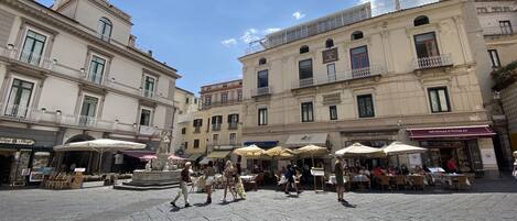 Una plaza histórica con adoquines, mesas al aire libre y arquitectura clásica.