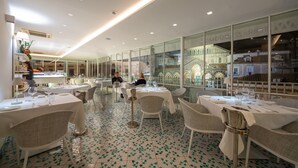 A restaurant with multiple tables set for dining, a tiled floor, and large windows offering views of buildings outside. - Terrazza Duomo (Amalfi)
