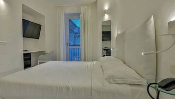 A modern hotel room with a large bed, a TV mounted on the wall, a desk with a chair, and a glass telephone.