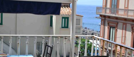 Un balcon avec une table et des chaises, donnant sur une zone côtière avec des bâtiments et la mer.