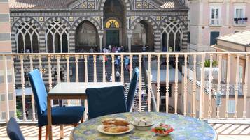 A balcony with a table set for two, overlooking a historic building with arches and a clock.