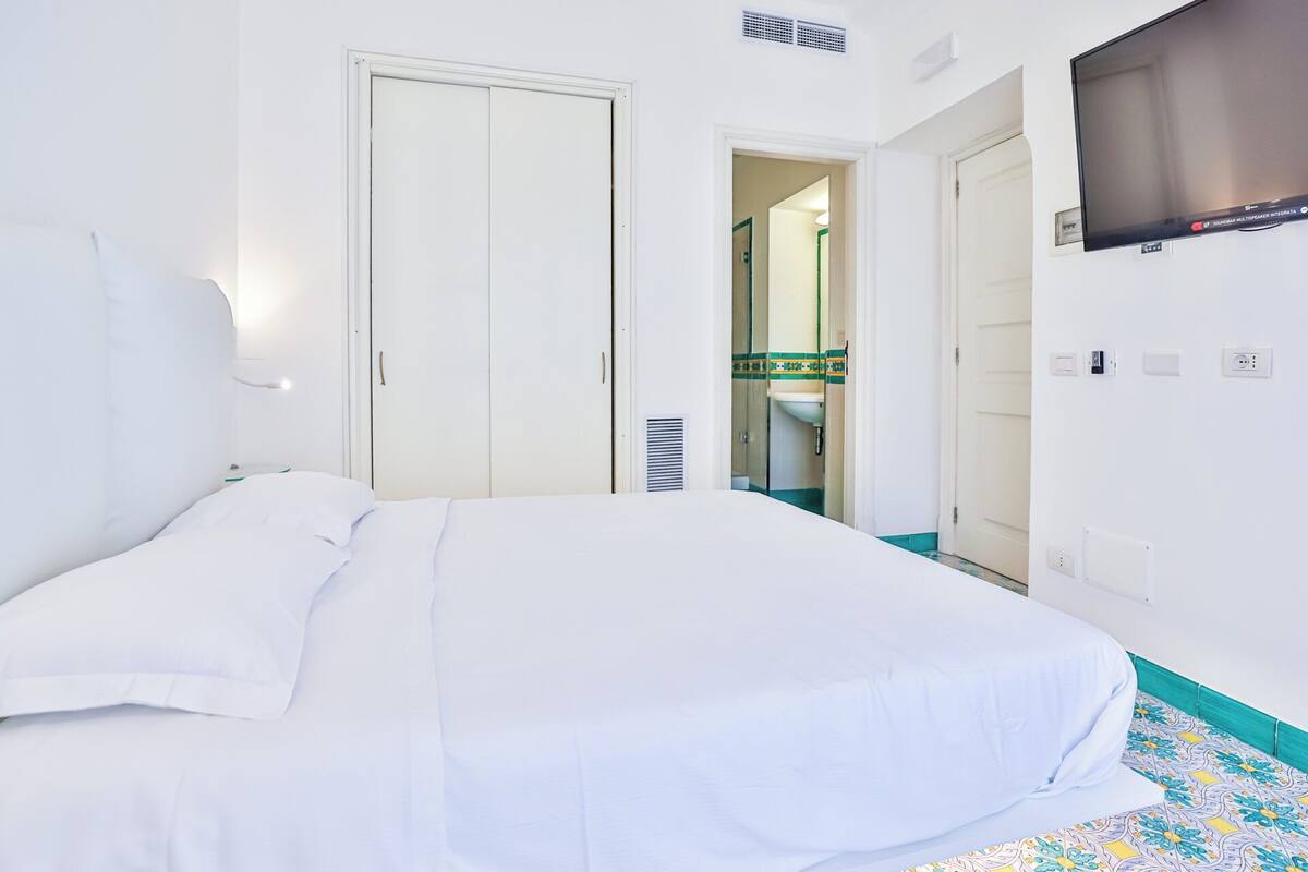 A hotel room with a bed, a TV mounted on the wall, and a bathroom visible through an open door.