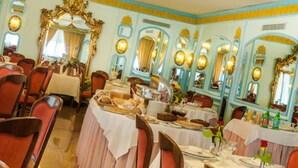 Une salle à manger avec plusieurs tables dressées pour les repas, des miroirs décoratifs et des lustres.