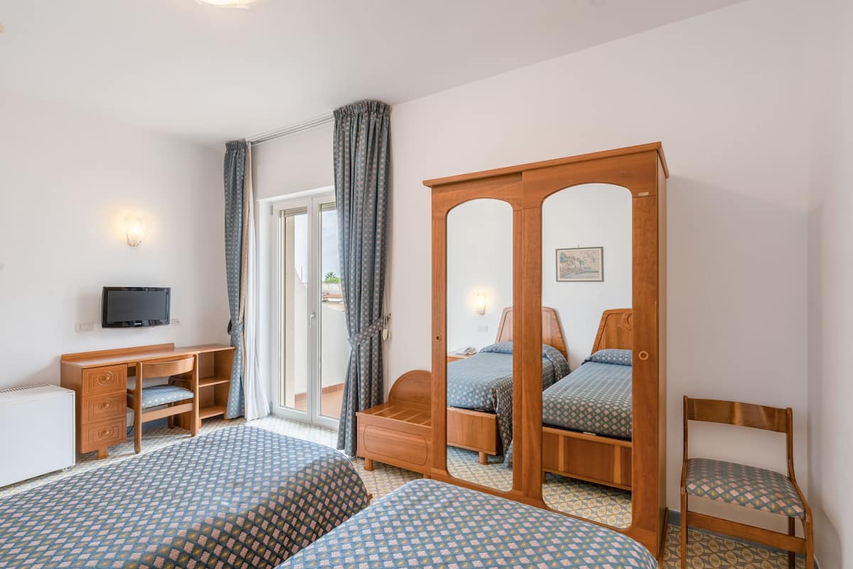 A bedroom with two beds, a wooden desk, a chair, a television, and a sliding glass door.