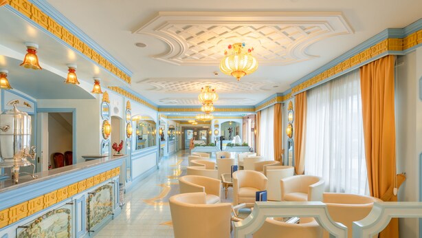 Un hall d’hôtel doté d’un long comptoir d’accueil, de plusieurs espaces aménagés avec des sièges et d’un plafond décoratif.