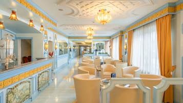 A hotel lobby with a long reception desk, multiple seating areas, and a decorative ceiling.