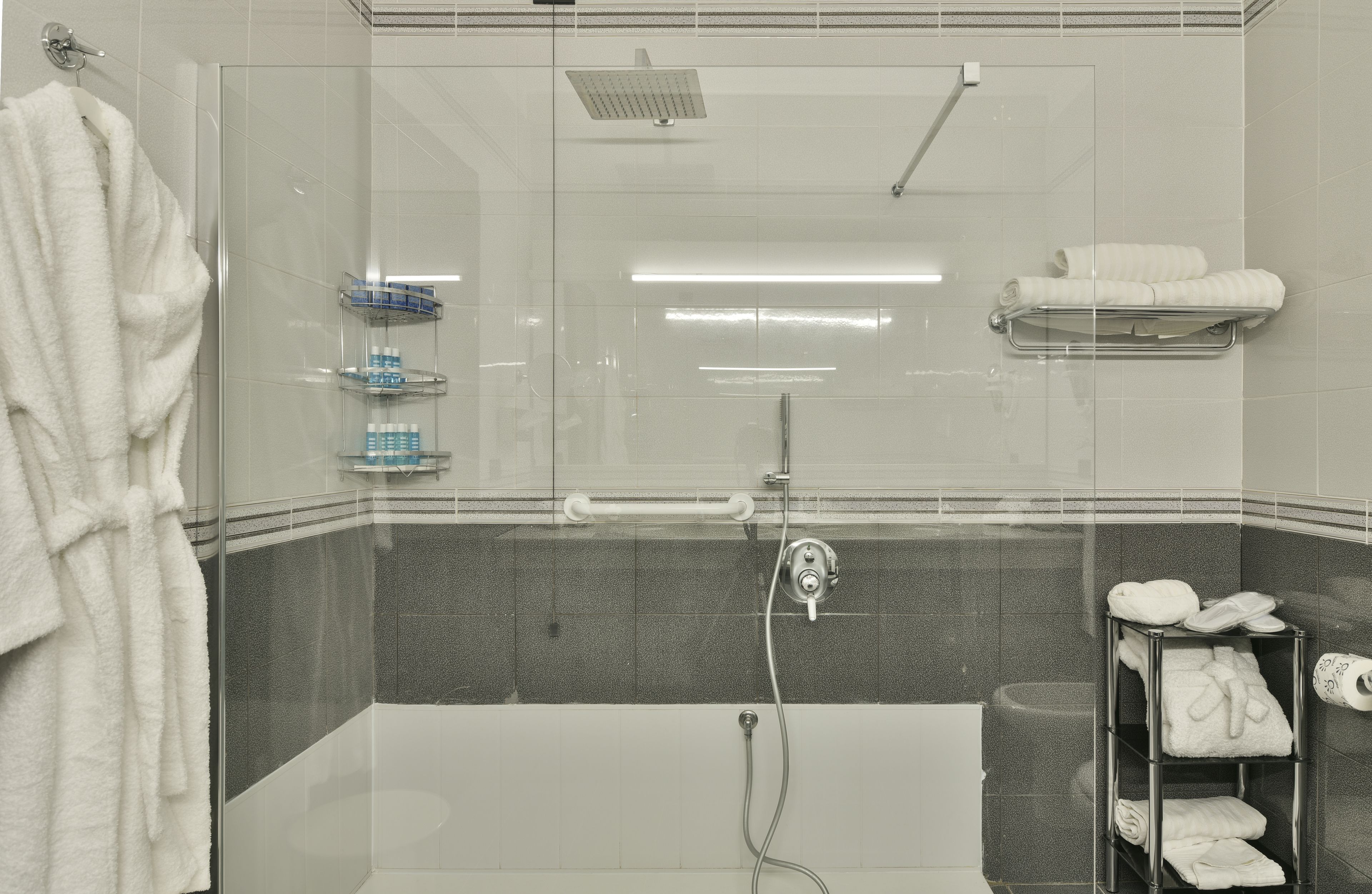 A modern bathroom with a glass-enclosed shower, a glass bathtub, and a towel rack with folded towels.
