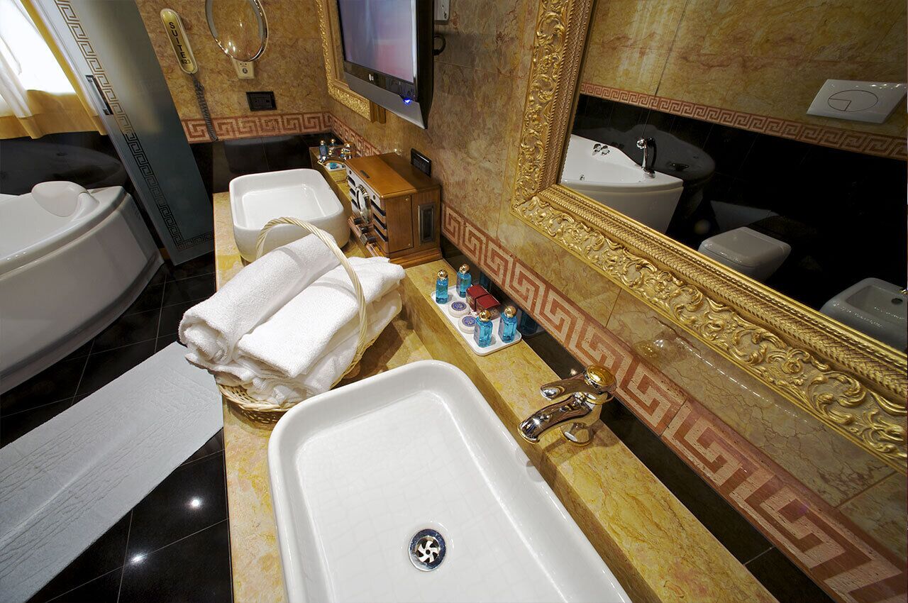 A bathroom with a large bathtub, two sinks, a vanity with toiletries, and a mirror with ornate gold detailing.