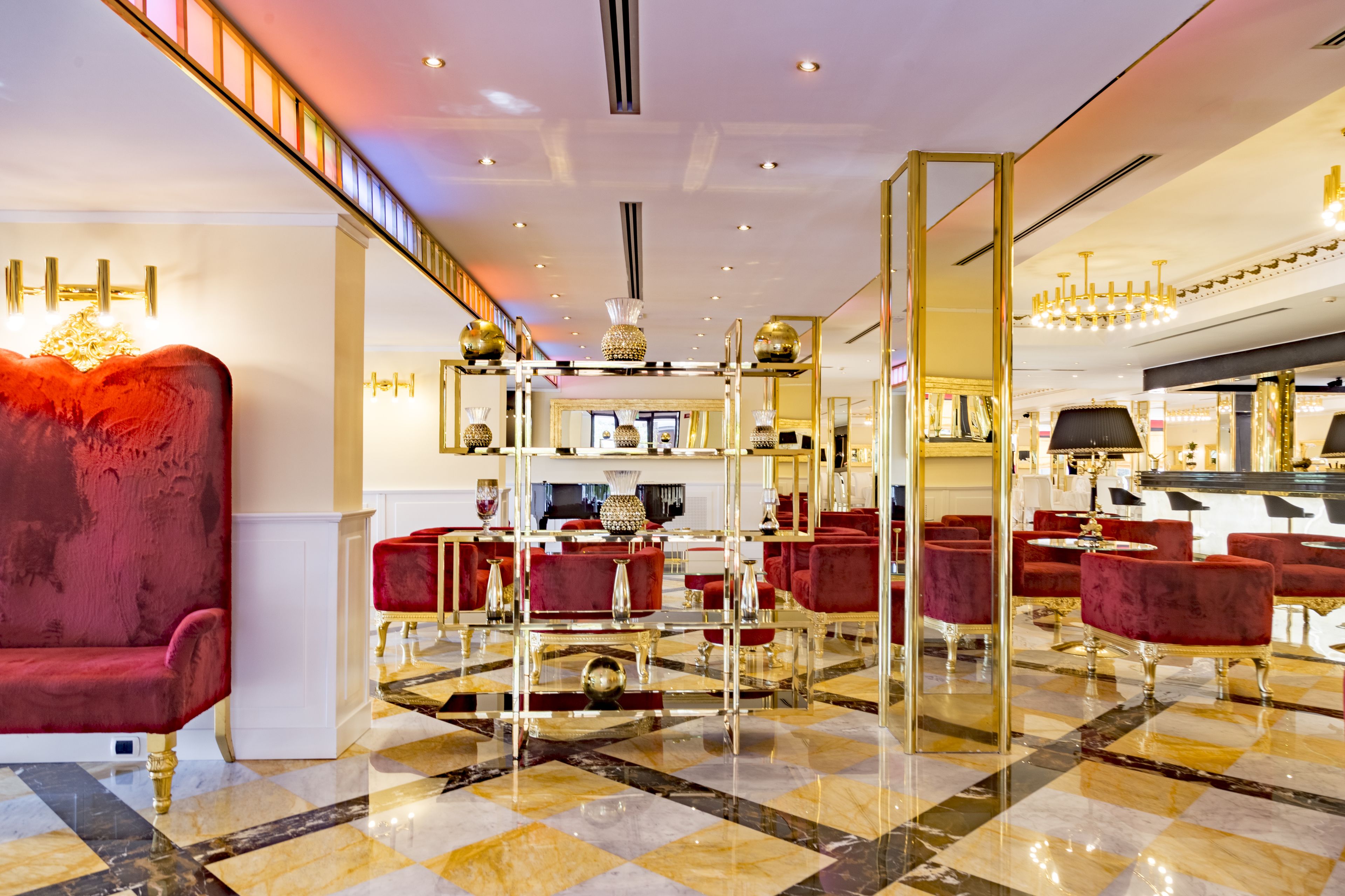 A luxurious lobby with red velvet sofas, a checkered marble floor, and gold accents.