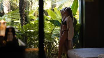 Una stanza con un'ampia finestra, un letto e vista su vegetazione tropicale.