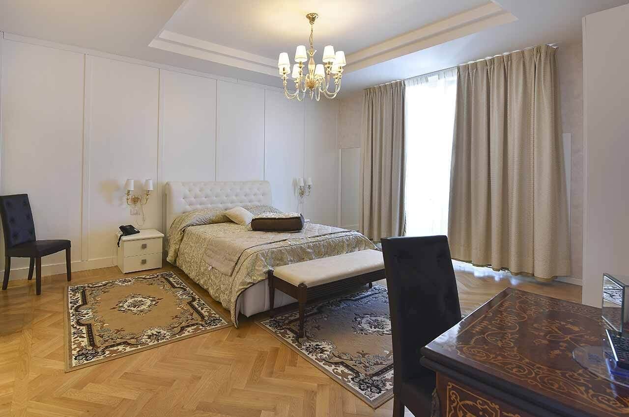 A bedroom with a large bed, a nightstand, a chair, a desk, and a chandelier.