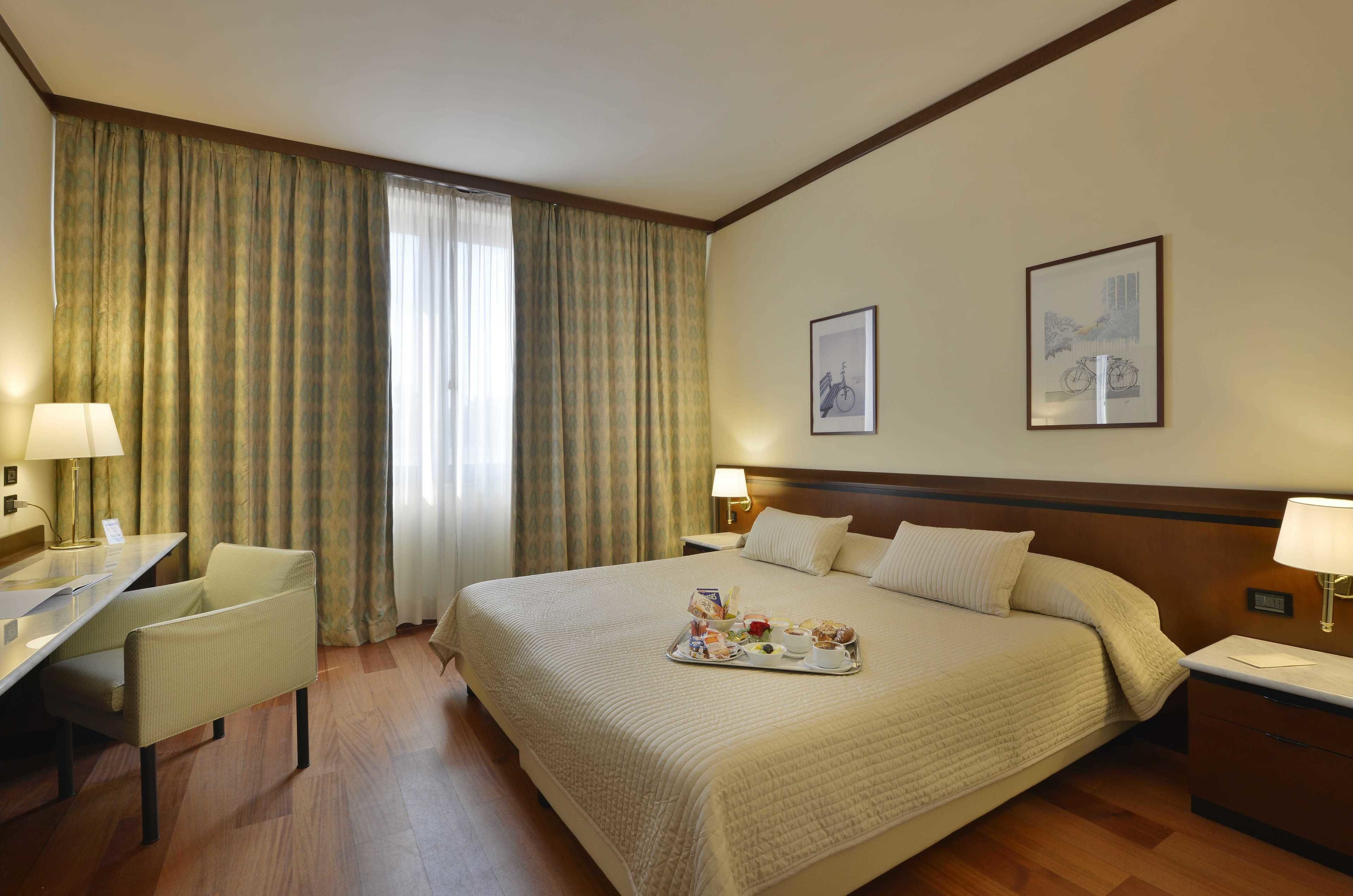 Une chambre d’hôtel avec un grand lit, un bureau, une chaise et un plateau contenant des articles pour le petit-déjeuner.