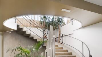 A spiral staircase with a modern design, a concrete wall, and a potted plant at the bottom.
