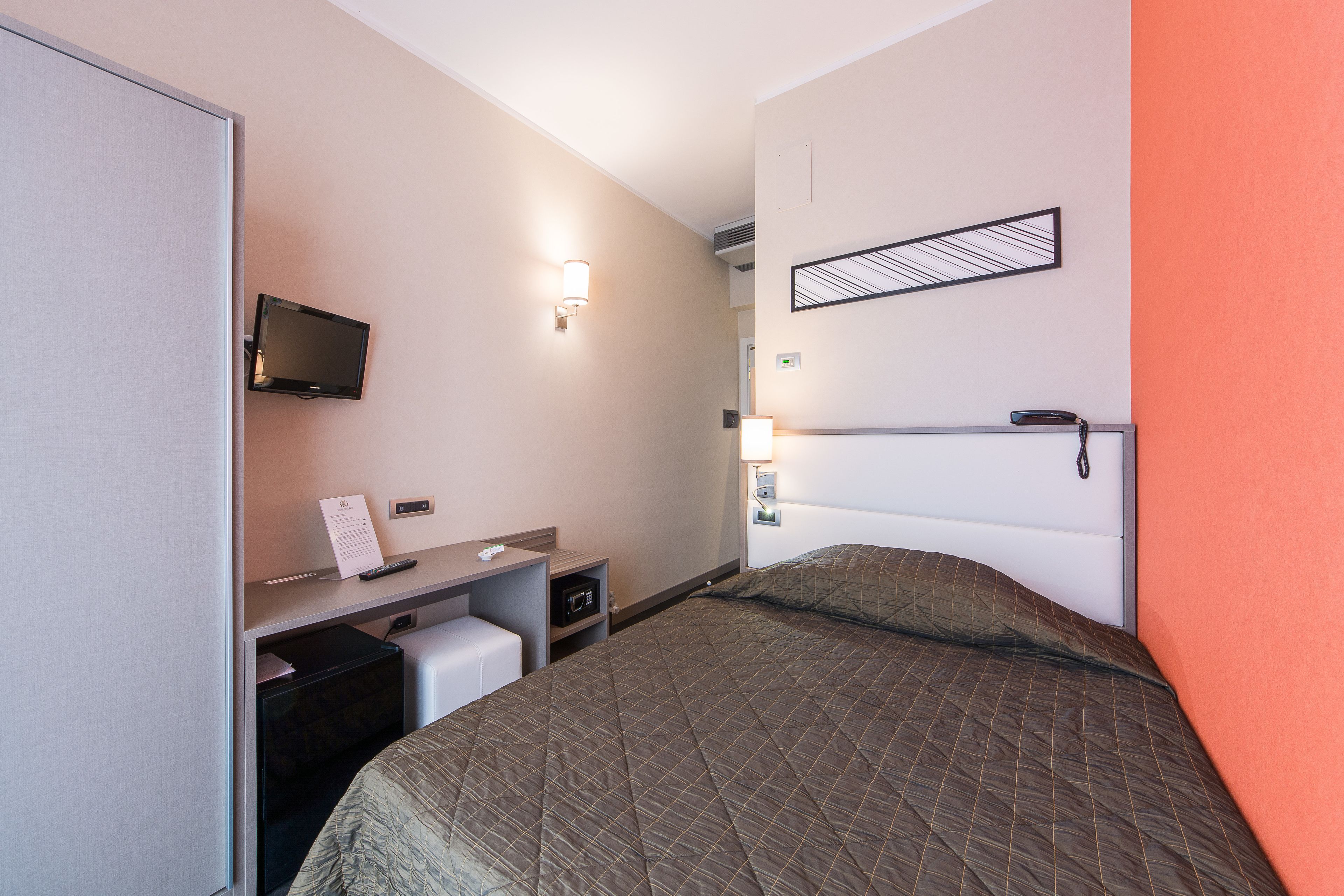 Una habitación de hotel con cama, escritorio, televisión y mesita de noche.
