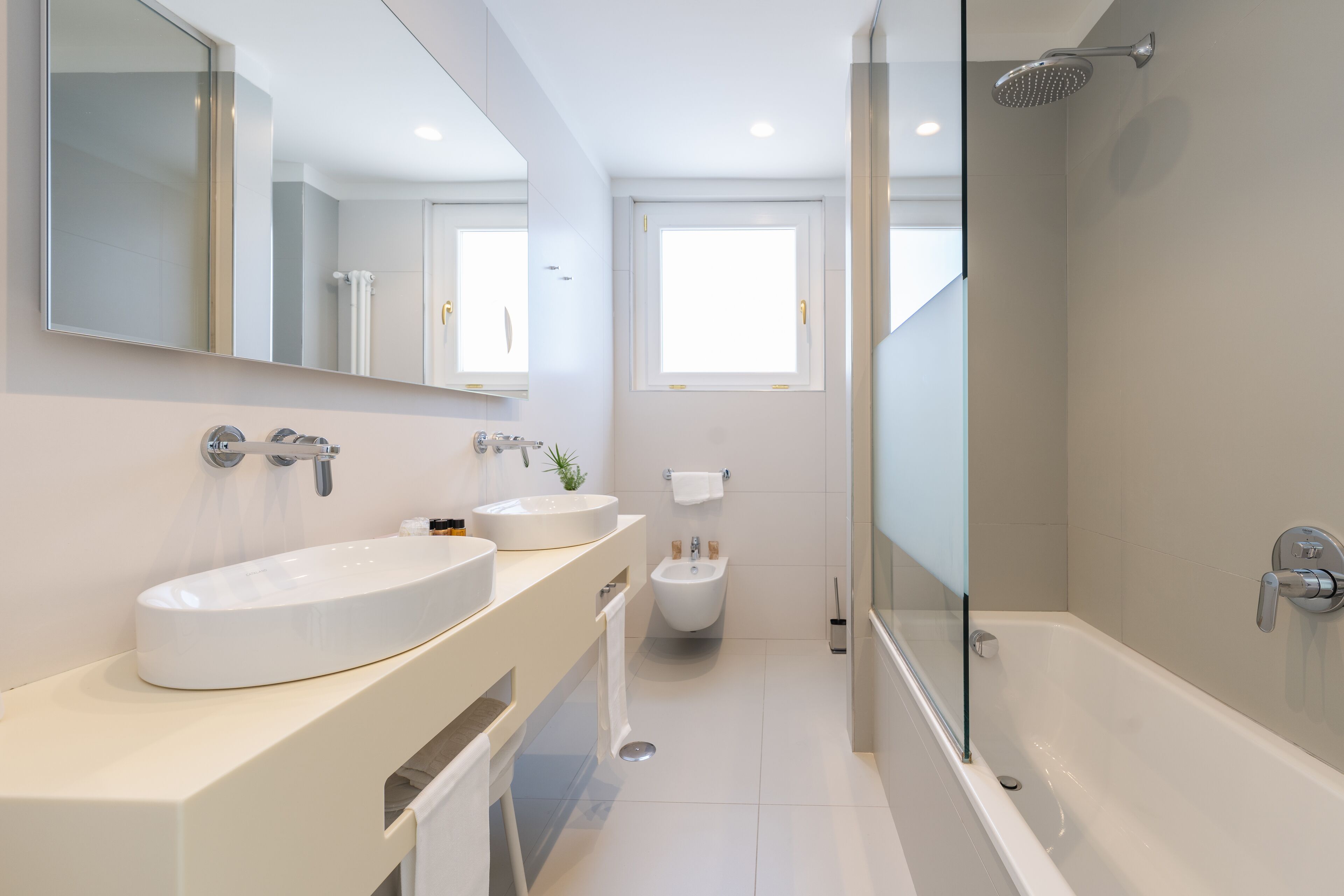 Un baño moderno con una bañera grande, dos lavamanos, un bidé y una cabina de ducha con paredes de vidrio.