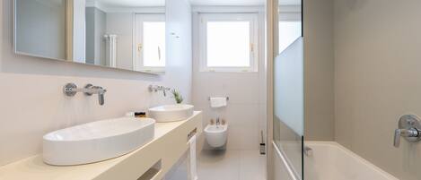 Un baño moderno con una bañera grande, dos lavamanos, un bidé y una cabina de ducha con paredes de vidrio.