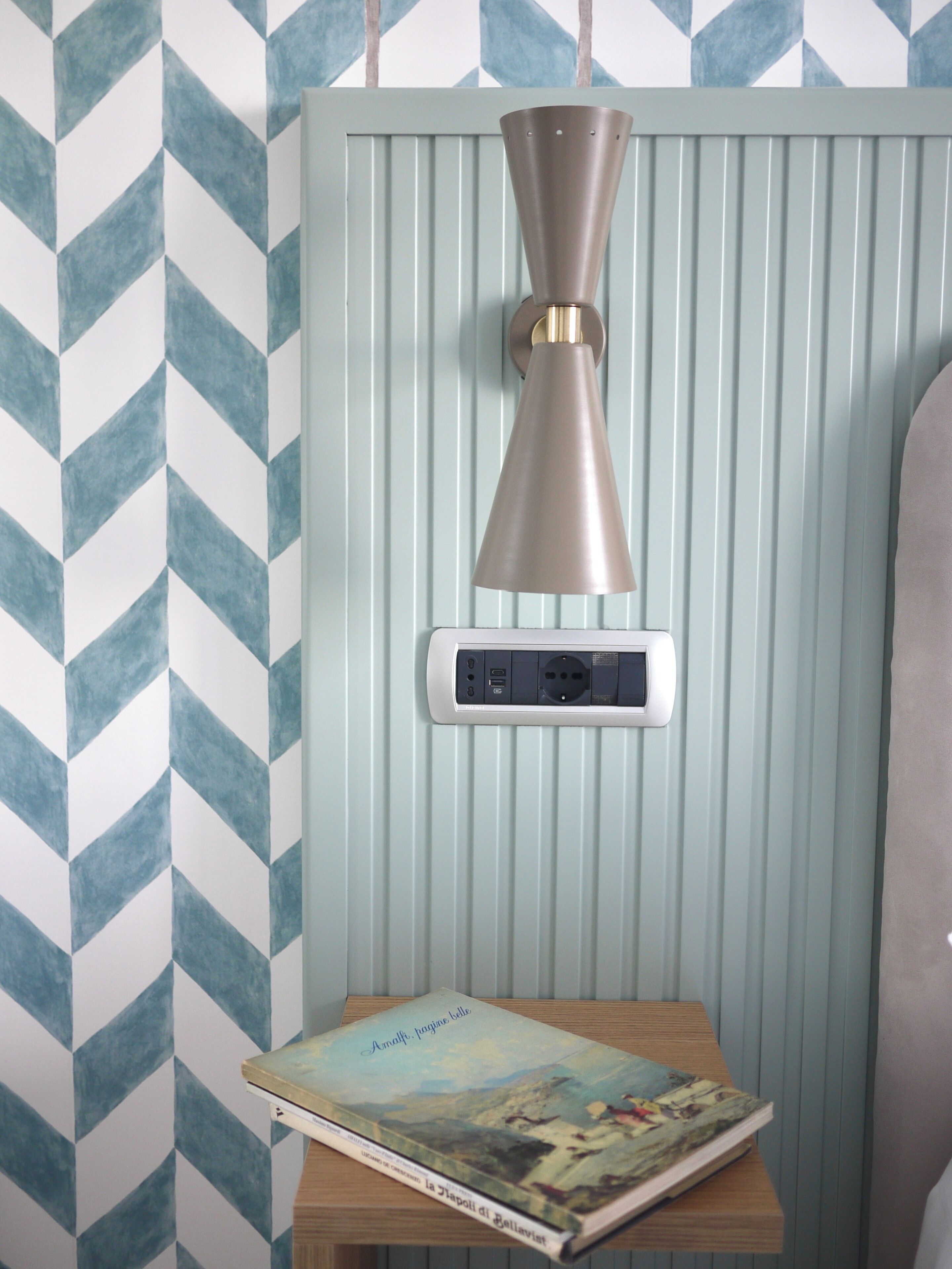 A room with a chevron-patterned wall, a pendant light fixture, a power strip, and a book titled "Amalfi, pagano bello".