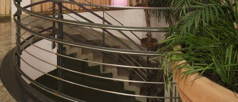A spiral staircase with a metal railing, a central column with a light fixture, and a potted plant to the right.