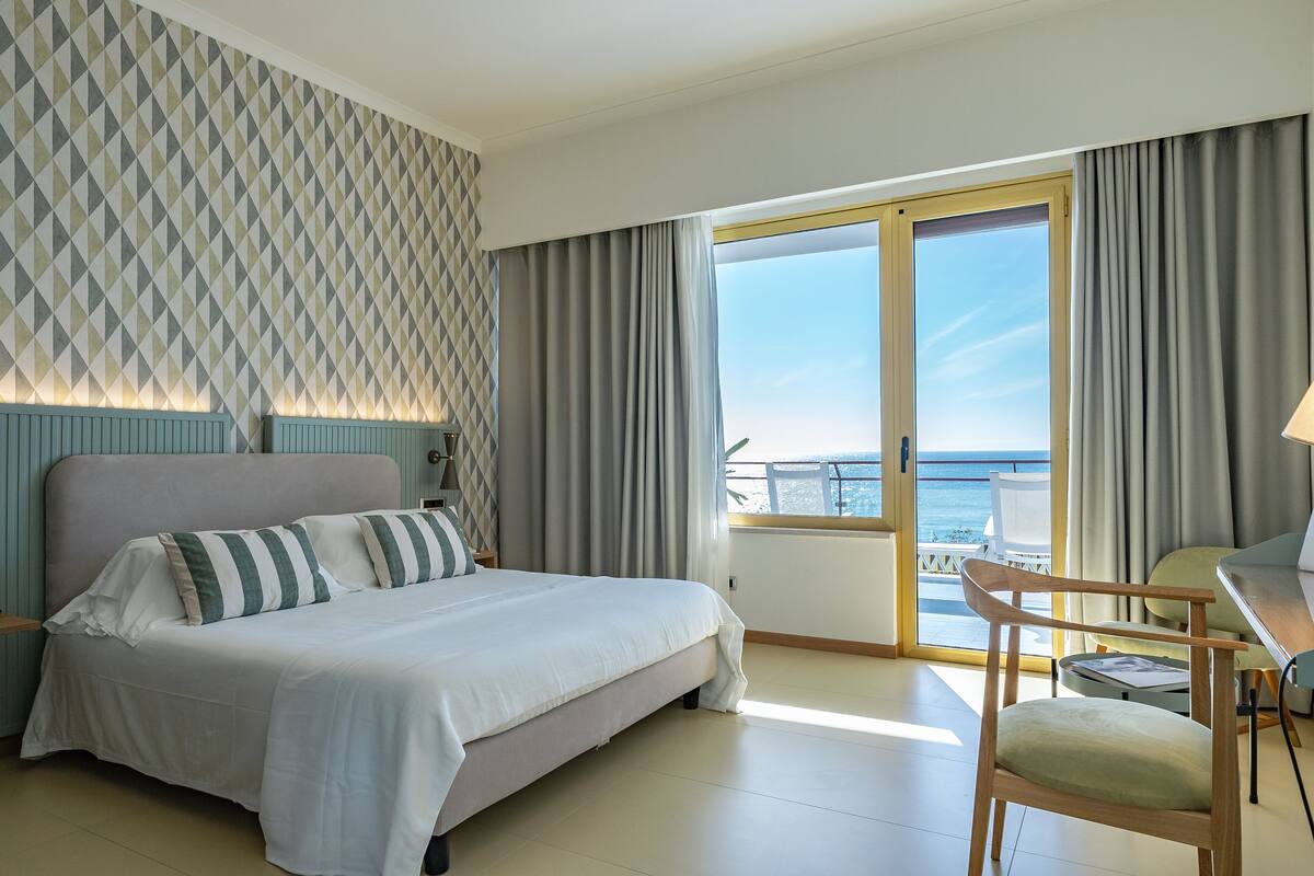 Ein Hotelzimmer mit Bett, Schreibtisch, Stuhl und Meerblick, inklusive Wand mit Muster.