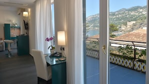 Habitación de hotel con balcón, escritorio con lámpara, silla y vistas a un pueblo costero.