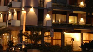Un hotel de varios pisos con balcones, un letrero que dice "RECINNA PALACE" y plantas de exterior.