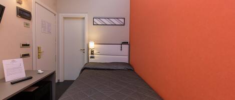 A hotel room with a bed, a desk with a remote control, a lamp, and a wall-mounted air conditioner.